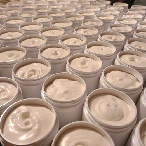 Multiple open white cosmetic jars filled with a thick, creamy off-white cream, arranged closely together in rows.